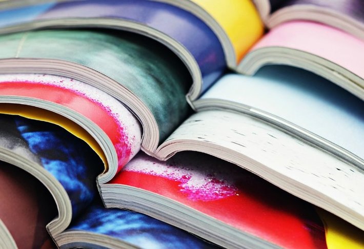 Verschillende opengeslagen tijdschriften liggen over elkaar. Veel verschillende kleuren zorgen voor een vrolijk beeld.